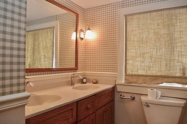 bathroom with a sink, toilet, and wallpapered walls