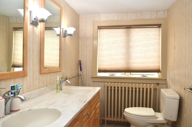 bathroom featuring radiator, double vanity, toilet, and a sink