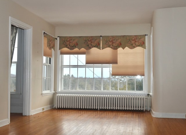 empty room with baseboards, radiator heating unit, and wood finished floors