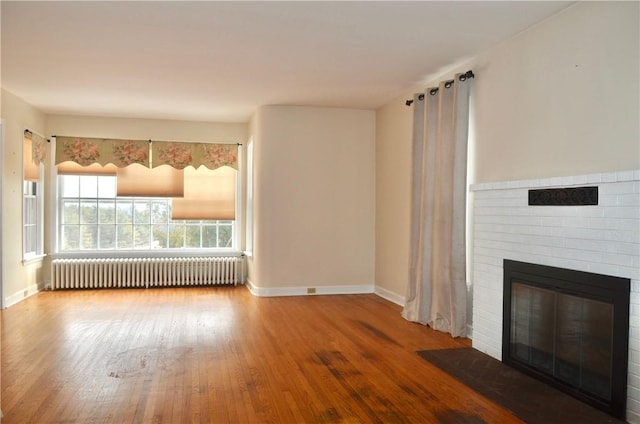 unfurnished living room featuring radiator, a fireplace, baseboards, and wood finished floors