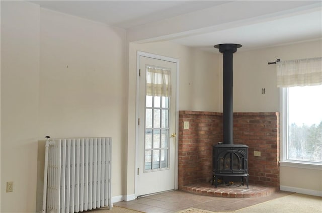 unfurnished living room with baseboards, light tile patterned floors, a wood stove, and radiator