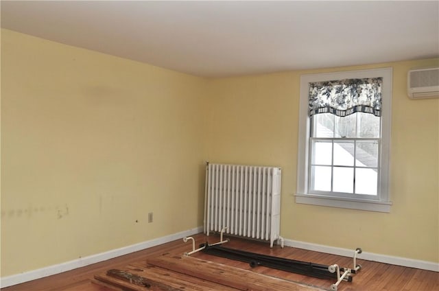 spare room featuring baseboards, an AC wall unit, wood finished floors, and radiator