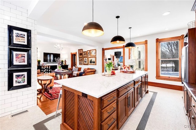 kitchen with light stone countertops, a kitchen island, and decorative light fixtures