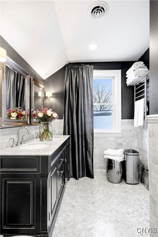 bathroom with lofted ceiling, vanity, and tile walls