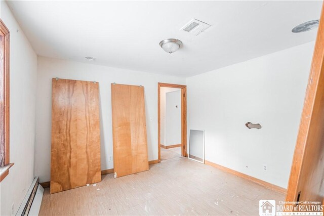 unfurnished bedroom featuring hardwood / wood-style flooring and baseboard heating