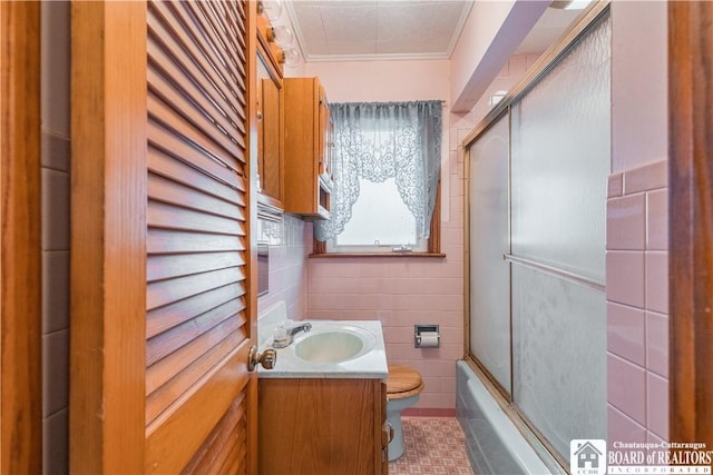 full bathroom with toilet, crown molding, shower / bath combination with glass door, tile walls, and vanity