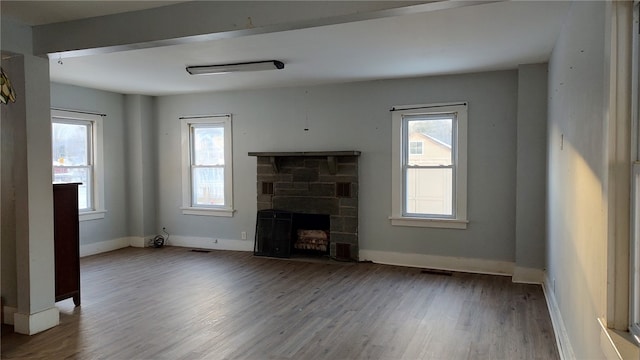 unfurnished living room featuring hardwood / wood-style flooring, plenty of natural light, and a stone fireplace