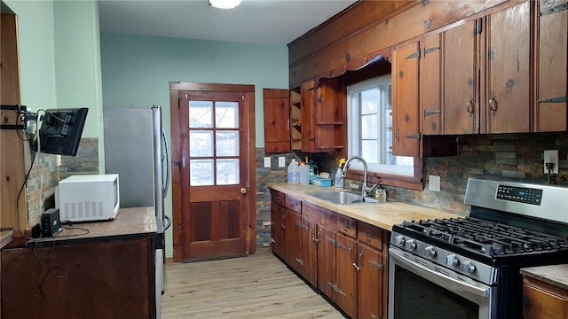 kitchen featuring gas range, sink, decorative backsplash, and light hardwood / wood-style flooring