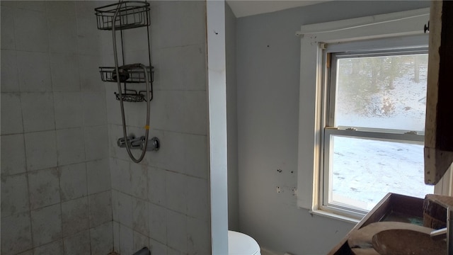 bathroom with tiled shower, a healthy amount of sunlight, toilet, and vanity