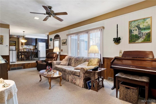 living room featuring ceiling fan, light colored carpet, and wooden walls