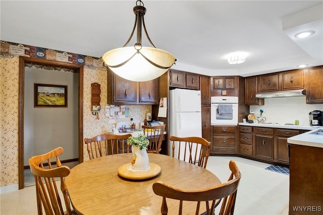 kitchen featuring hanging light fixtures, tasteful backsplash, dark brown cabinets, and white appliances