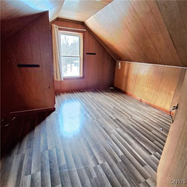 additional living space with vaulted ceiling, wooden walls, and light wood-type flooring