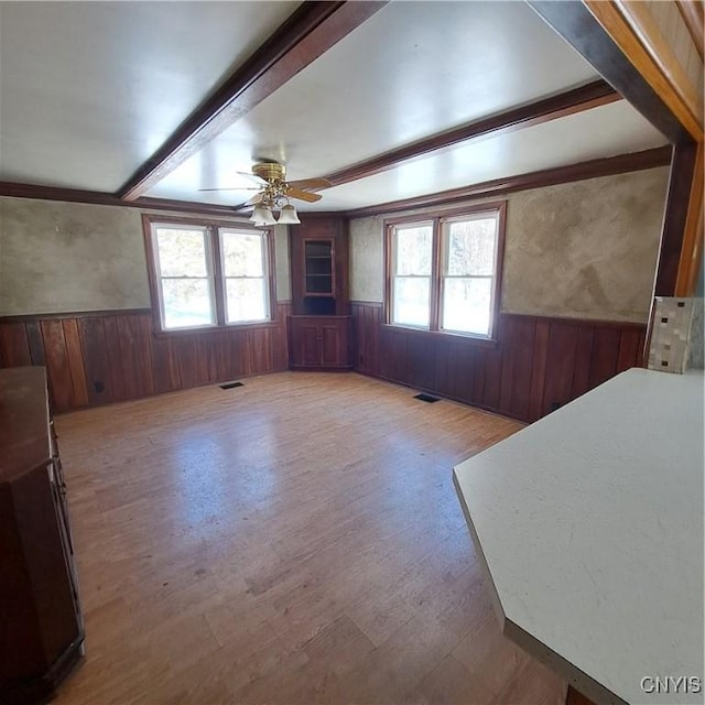 unfurnished living room featuring hardwood / wood-style flooring, ceiling fan, beam ceiling, and wood walls