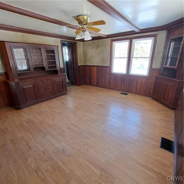 unfurnished living room with ceiling fan, beam ceiling, wood walls, and light wood-type flooring