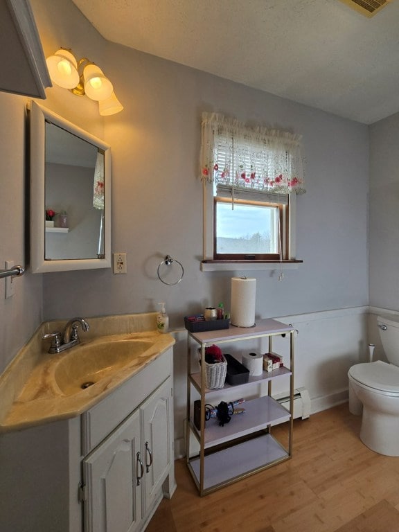 bathroom with vanity, hardwood / wood-style flooring, toilet, and baseboard heating