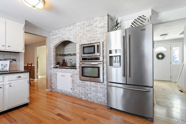 kitchen with light hardwood / wood-style flooring, dark stone counters, white cabinets, and appliances with stainless steel finishes