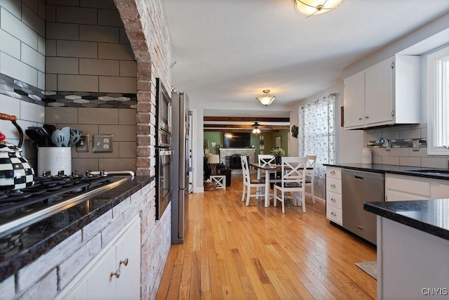 kitchen with appliances with stainless steel finishes, a wealth of natural light, white cabinets, decorative backsplash, and light hardwood / wood-style flooring