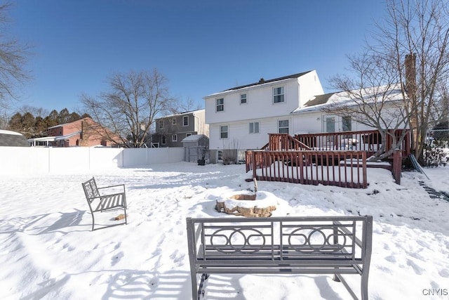 snow covered rear of property featuring a wooden deck and a storage unit