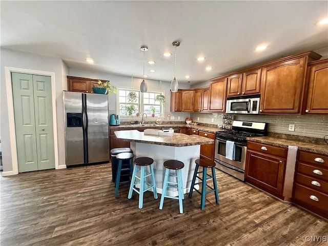 kitchen featuring a breakfast bar area, dark wood-type flooring, appliances with stainless steel finishes, a kitchen island, and decorative light fixtures