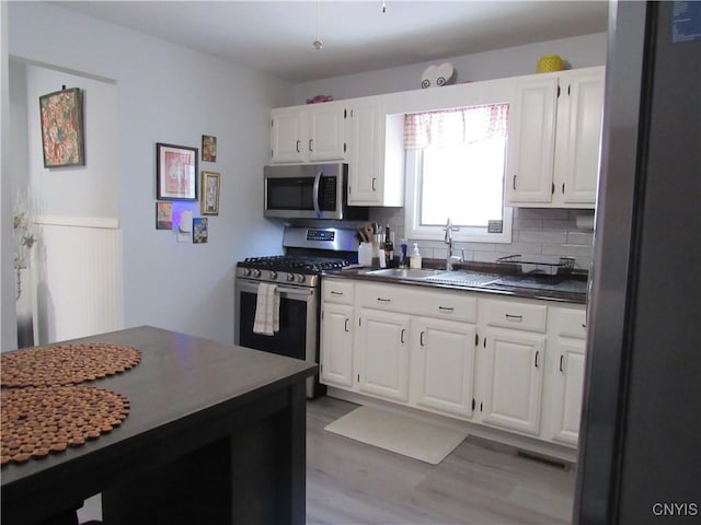 kitchen featuring sink, appliances with stainless steel finishes, white cabinetry, tasteful backsplash, and light hardwood / wood-style floors