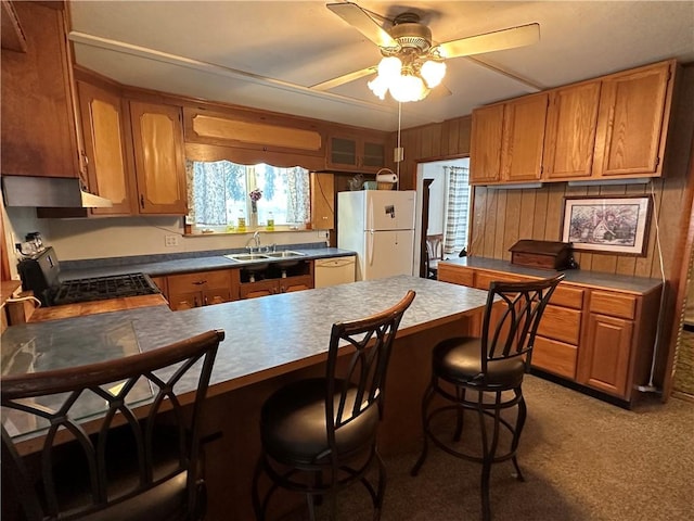 kitchen featuring wooden walls, white appliances, ceiling fan, a breakfast bar, and sink