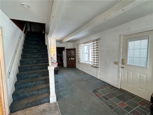 entryway with beam ceiling, wood walls, and dark carpet