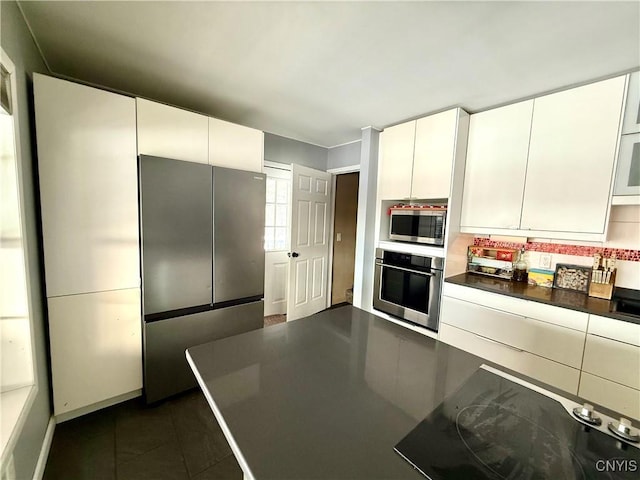 kitchen featuring tasteful backsplash, dark tile patterned floors, white cabinets, and appliances with stainless steel finishes