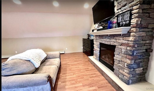 living room featuring vaulted ceiling, a stone fireplace, a baseboard heating unit, and light wood-type flooring