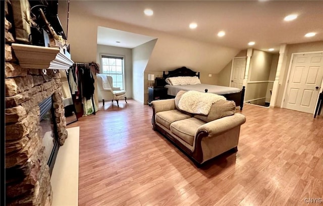 bedroom featuring vaulted ceiling, a stone fireplace, and light wood-type flooring