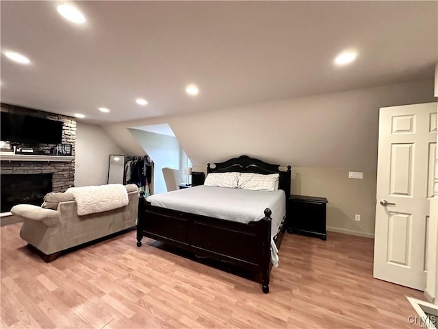 bedroom featuring vaulted ceiling, a stone fireplace, and light hardwood / wood-style floors