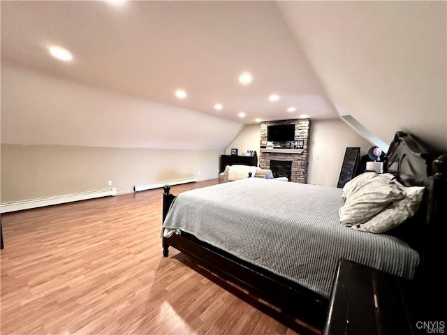 bedroom featuring a baseboard radiator, vaulted ceiling, a stone fireplace, and light wood-type flooring