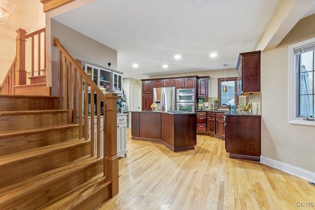 kitchen featuring light hardwood / wood-style flooring, dark stone countertops, appliances with stainless steel finishes, a kitchen island, and backsplash