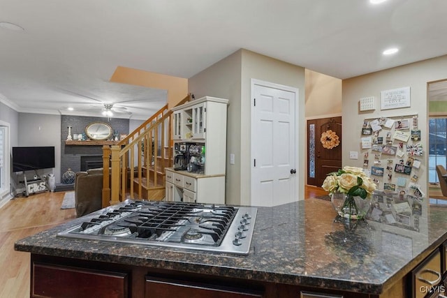 kitchen featuring dark stone countertops, white cabinets, stainless steel gas cooktop, ceiling fan, and a brick fireplace