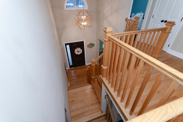 stairs with a towering ceiling, a chandelier, and hardwood / wood-style floors