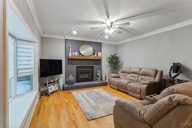 living room featuring a brick fireplace, crown molding, wood-type flooring, and ceiling fan