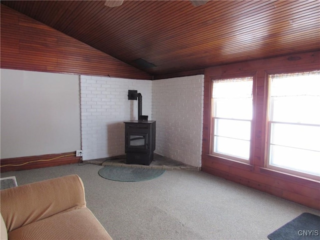 living room featuring vaulted ceiling, brick wall, carpet floors, a wood stove, and wood ceiling