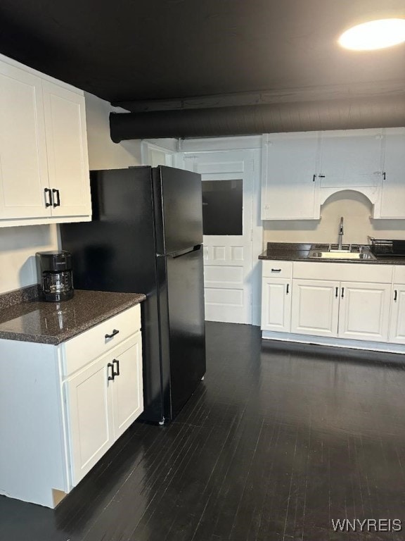 kitchen with sink, white cabinetry, black fridge, dark hardwood / wood-style flooring, and dark stone counters