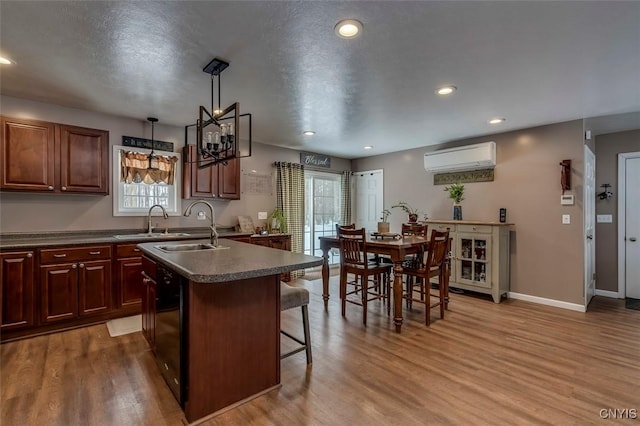 kitchen with a wall mounted AC, a kitchen breakfast bar, an island with sink, pendant lighting, and hardwood / wood-style floors