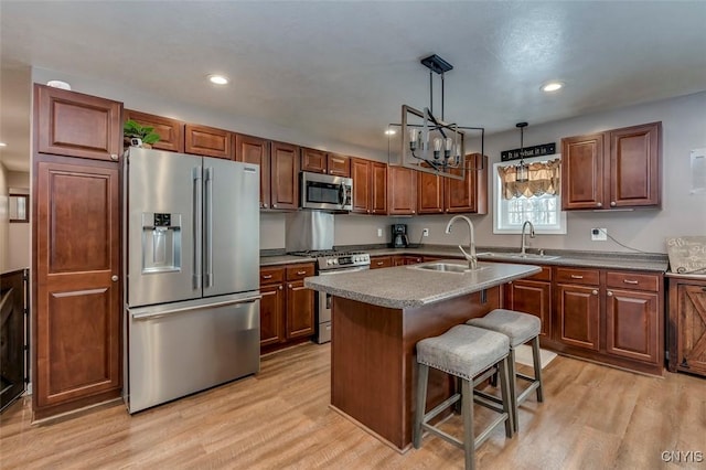 kitchen with pendant lighting, sink, appliances with stainless steel finishes, a center island with sink, and a kitchen bar