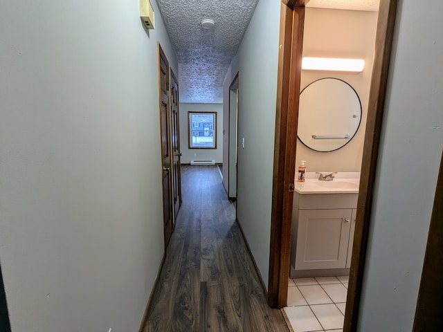 hallway featuring sink, hardwood / wood-style floors, a textured ceiling, and a baseboard heating unit