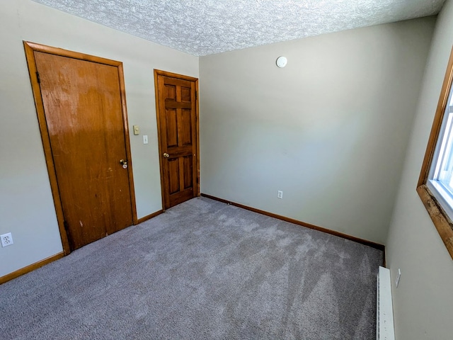 carpeted empty room featuring a textured ceiling and baseboard heating