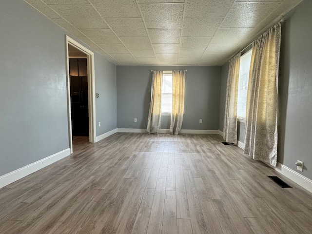 spare room with a paneled ceiling and light wood-type flooring