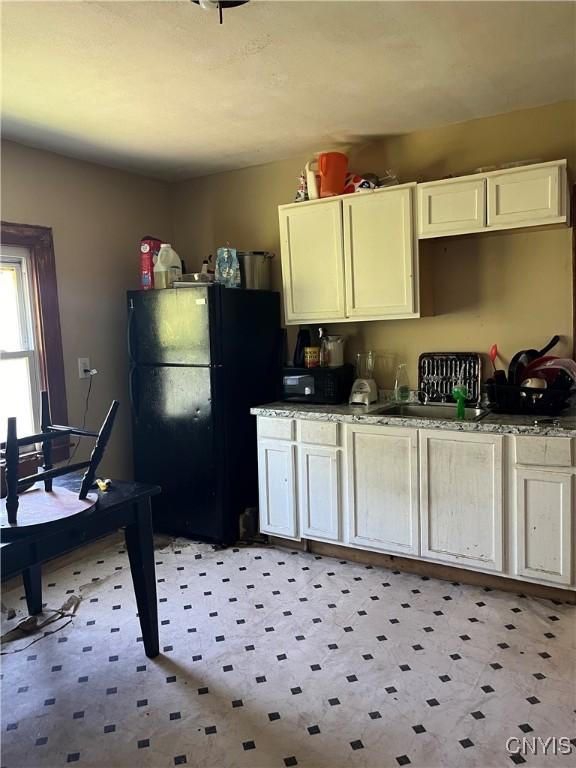 kitchen with black refrigerator, sink, and light stone counters