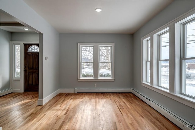 foyer entrance with a baseboard heating unit, a wealth of natural light, and light hardwood / wood-style floors