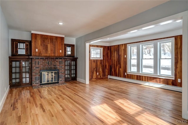 unfurnished living room featuring a baseboard radiator, a fireplace, light hardwood / wood-style floors, and wood walls