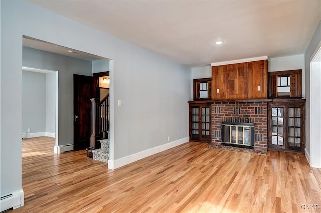 unfurnished living room with baseboard heating, a fireplace, and light hardwood / wood-style floors