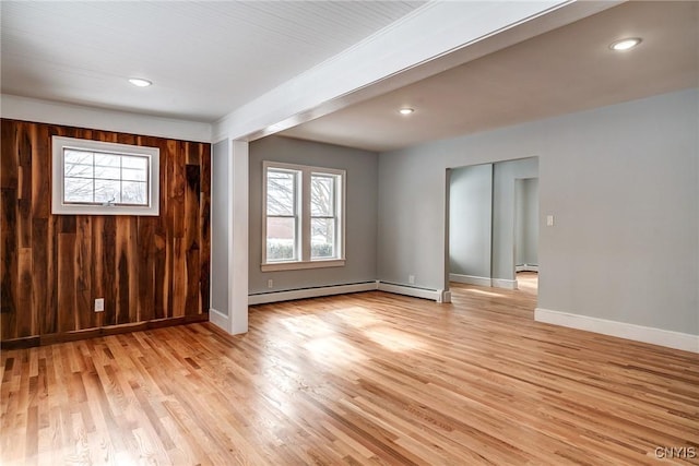 empty room with a baseboard heating unit, wood walls, and light wood-type flooring