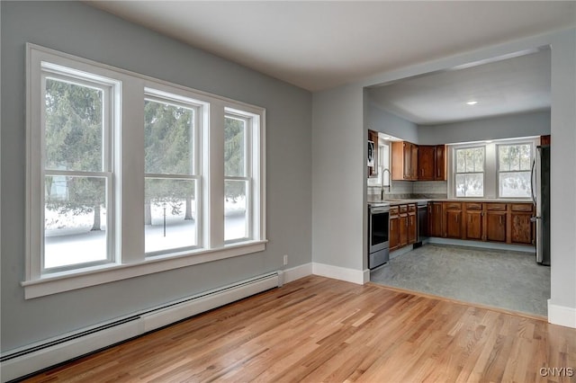 kitchen with a baseboard heating unit, light wood-type flooring, sink, and appliances with stainless steel finishes