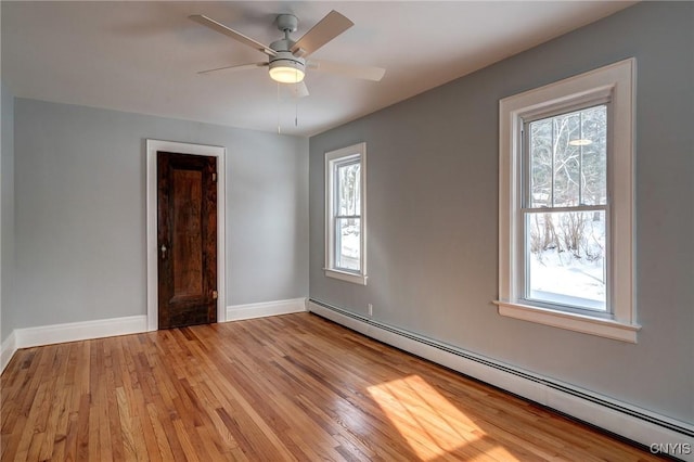 empty room featuring ceiling fan, a baseboard heating unit, and light wood-type flooring