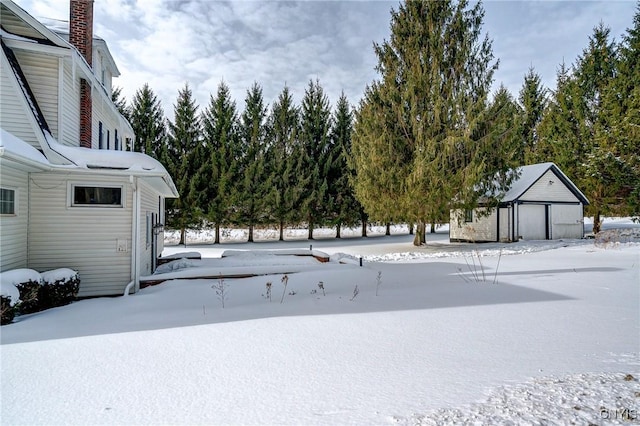 snowy yard featuring a garage and an outdoor structure